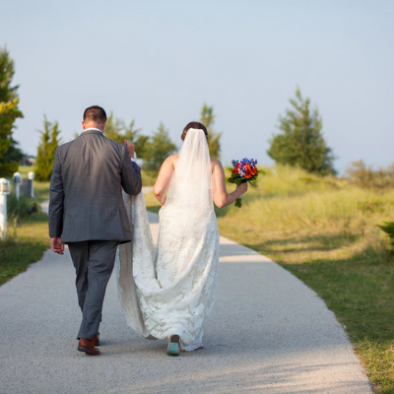 BRIDE AND GROOM WALK ALONG BEACH AT BLUE HARBOR RESORT WEDDING